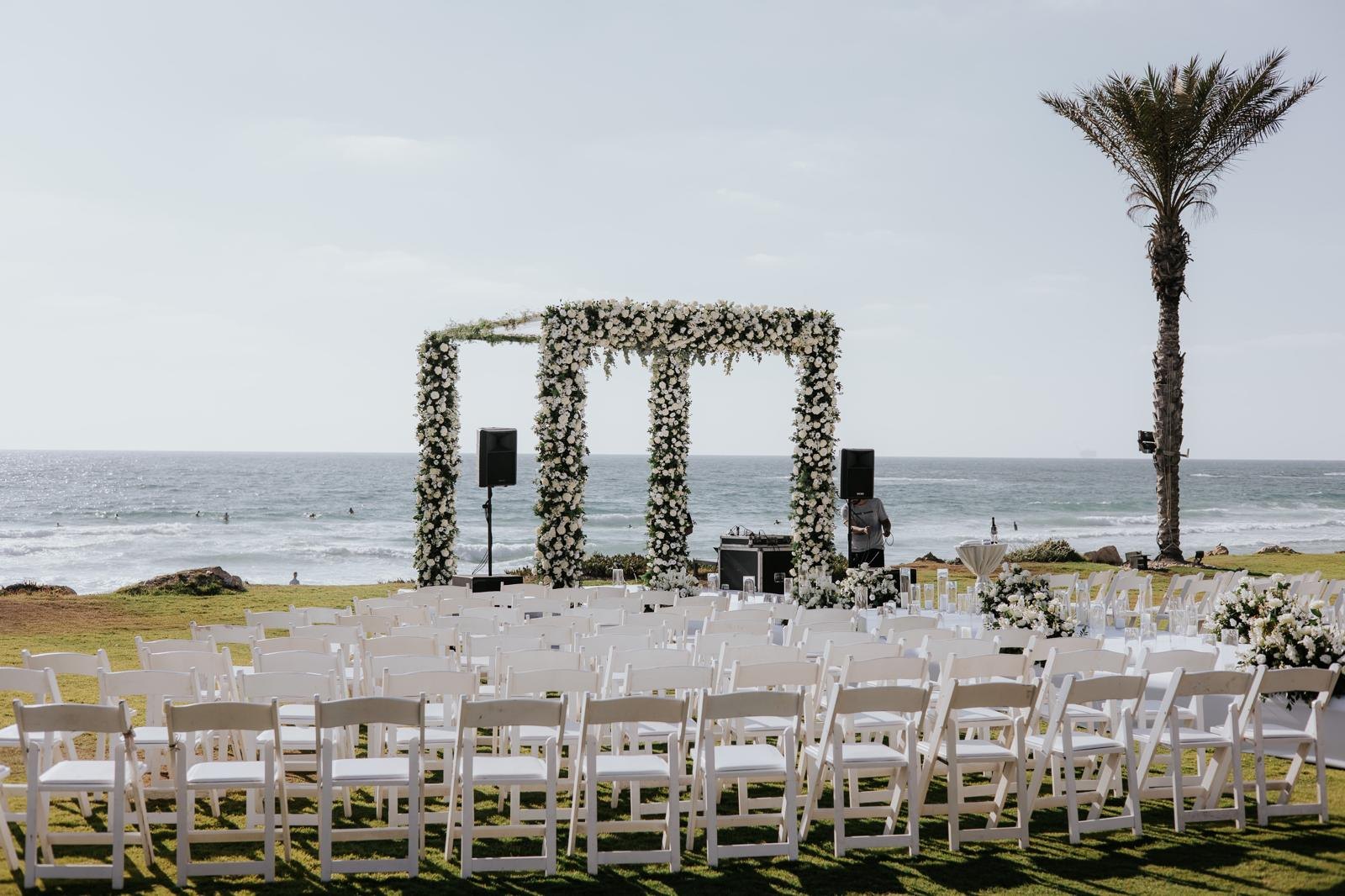 Arche de fleurs blanches face à la mer et chaises blanches, cérémonie de mariage organisée en Israël